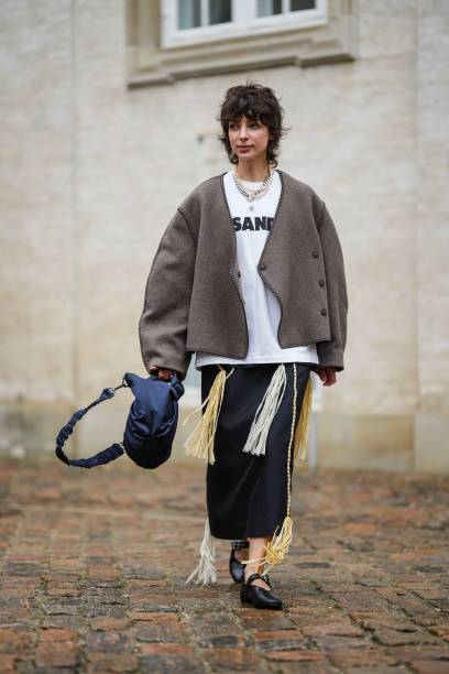 Guest wears a silver large chain necklace, a white pearls necklace, a white with black logo print pattern t-shirt from Jil Sander, a dark gray...