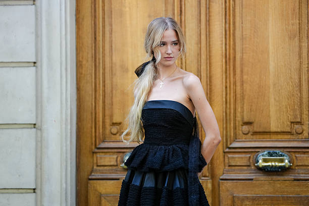 Guest wears a strapless black dress featuring a textured, boucle-like fabric. The dress has a fitted bodice with a peplum detail at the waist and a...