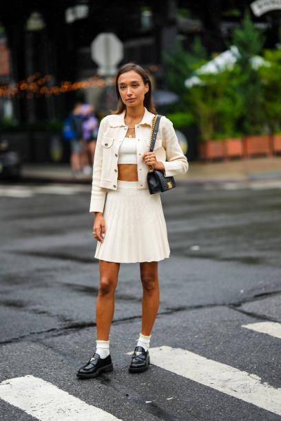 Guest wears a white shoulder-off / cropped top, a white latte buttoned jacket, a white latte embossed ribbed short skirt, a black shiny leather Boy...