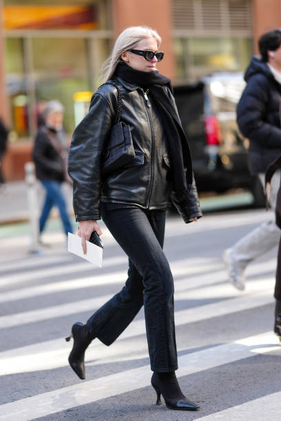 Guest wears Alaia sunglasses, a black scarf, a black leather jacket, black denim pants / jeans , pointed boots, outside Calvin Klein, during New York...