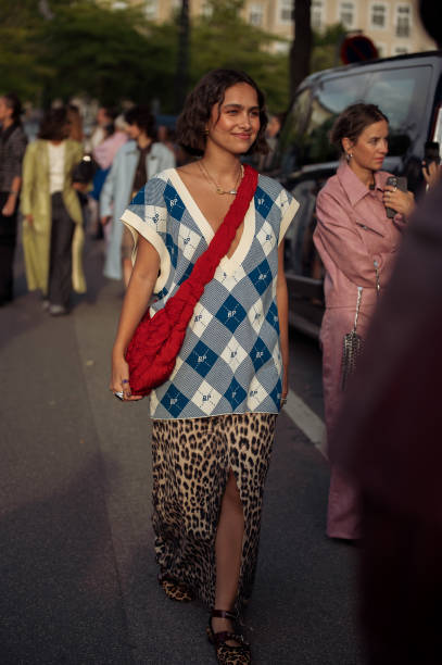 Guest wears animal print long skirt with split, white and blue BP checkered vest and red shoulder bag outside the Baum und Pferdgarten show during...