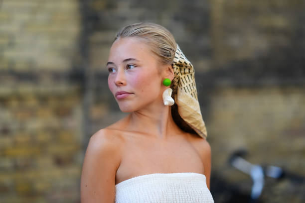 Guest wears beige black pattern head scarf, bright green and white earrings, white sheer mesh tube top, outside Deadwood, during the Copenhagen...