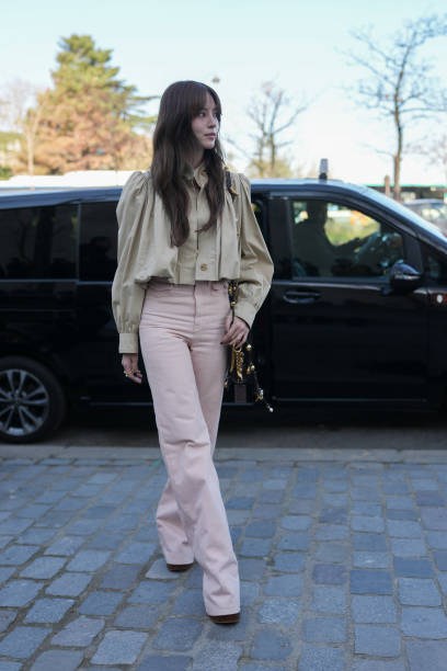 Guest wears beige cropped trench coat Chloe jacket, light pink high waisted loose Chloe denim jean pants, shiny black leather bag, gold rings,...