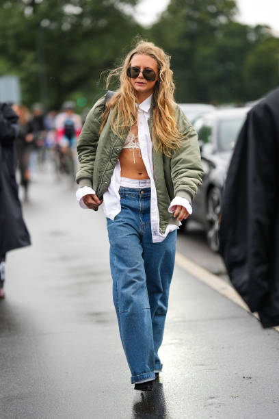 Guest wears black aviator sunglasses, a white shirt, a white lace print pattern V-neck bra underwear, a pale khaki bomber coat, white silk panties...