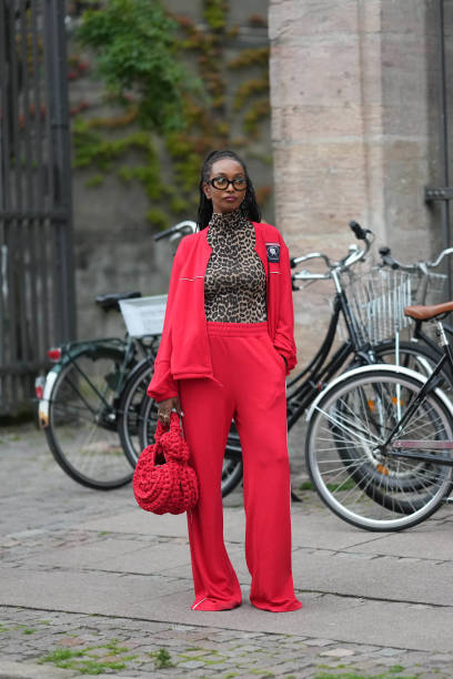 Guest wears black glasses, a brown / beige and black leopard print pattern turtleneck t-shirt, a neon red zipper sport sweater, matching neon red...