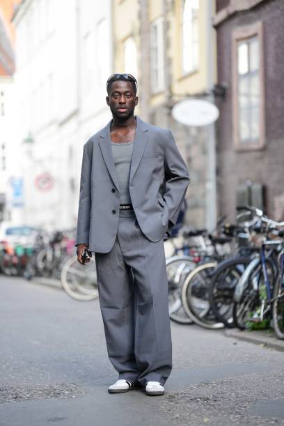 Guest wears black sport sunglasses, a gray tank-top, a gray oversized blazer jacket, matching gray large suit pants, white leather and gray suede...
