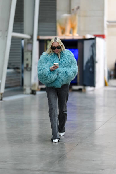 Guest wears black sunglasses, a blue faux fur fluffy jacket, black denim jeans / pants, white leather pointed shoes, outside BlueMarble, during the...