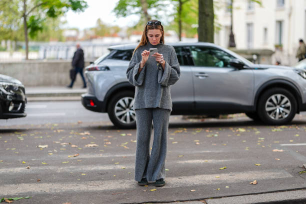Guest wears black sunglasses, a grey wool turtleneck pullover, matchings pants, dark green sneakers shoes, during Womenswear Spring/Summer 2025 as...