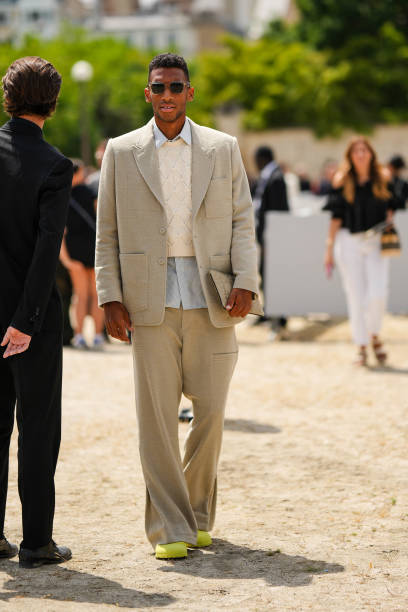 Guest wears black sunglasses, a pale blue shirt, a white latte braided wool gilet, a beige blazer jacket, matching beige suit pants, neon yellow felt...