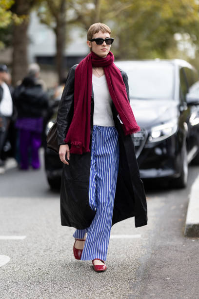 Guest wears black sunglasses, a red scarf, a white sweater, a brown leather trench, blue and white striped trousers and red leather maryjane shoes...