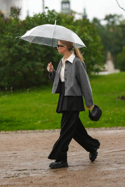 Guest wears black sunglasses, a white latte shirt, a gray blazer jacket, a black pleated / accordion short skirt, a black shiny leather handbag from...