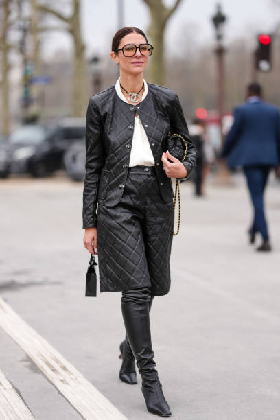 Guest wears black sunglasses, black silver Chanel choker necklace, white shirt, shiny black quilted Chanel leather jacket, gold bracelets, a gold...