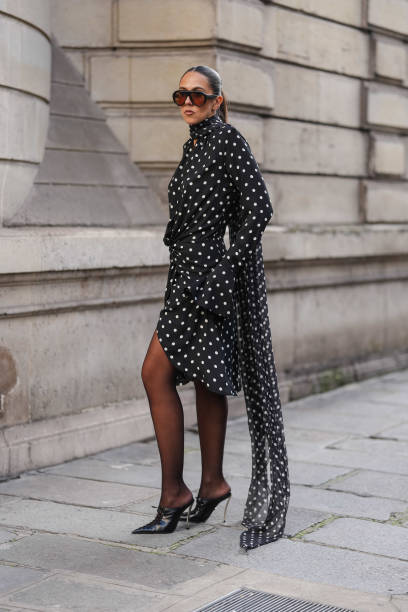 Guest wears black sunglasses, black white polka dotted sheer mesh high neck long sleeve mini dress, dark brown sheer mesh tights, shiny black pointed...
