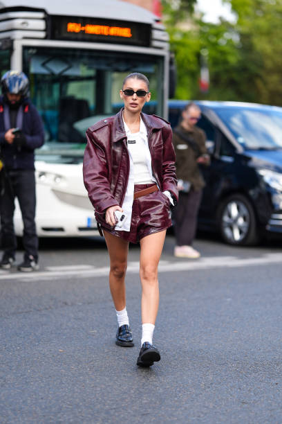 Guest wears black sunglasses, cream tank top, white unbuttoned long sleeve shirt, shiny dark red oversized biker leather jacket, dark brown leather...