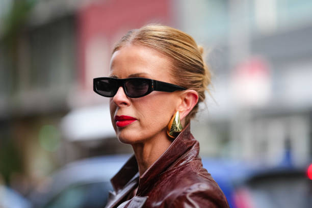 Guest wears black sunglasses, gold earrings, shiny dark brown blazer leather jacket, outside Monse, during the New York Fashion week Fall/Winter 2025...