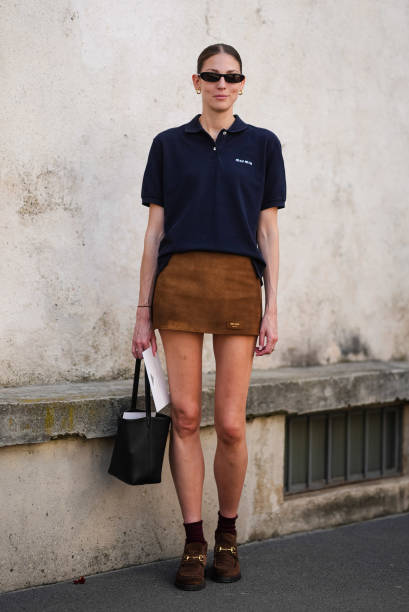 Guest wears black sunglasses, gold hoop earrings, black three buttoned short sleeve cotton shirt, brown suede mini skirt, silver rings, black small...
