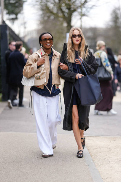 Guest wears black sunglasses, gold pearl earrings, dark green shirt, navy blue jacket, light brown cropped Lacoste coat, white Lacoste leather bag,...