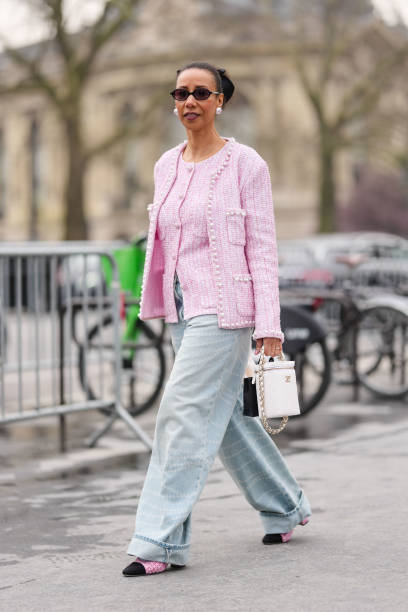 Guest wears black sunglasses, pearl Chanel earrings, black bow hair accessory, white light pink pattern buttoned tweed Chanel blazer jacket, white...