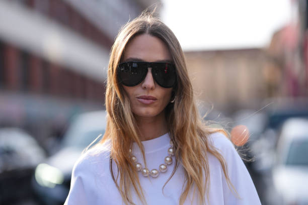 Guest wears black sunglasses, pearl necklace, white oversized black print Moschino shirt, outside Moschino, during the Milan Fashion week Women's...