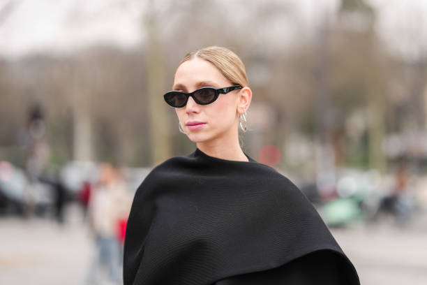 Guest wears black sunglasses, silver hoop earrings, black cape, outside Chanel, during the Paris Fashion week Women's Fall/Winter 2025-2026 on March...