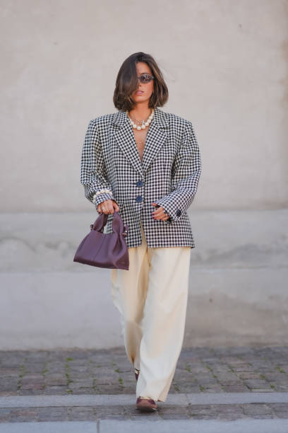 Guest wears black sunglasses, silver necklace, white beaded necklace, black and white pattern oversized blazer jacket, silver rings, white pearl...