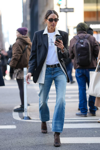 Guest wears black sunglasses, white Calvin Klein Jeans print t-shirt, cream unbuttoned long sleeve shirt, black blazer jacket, black leather belt,...