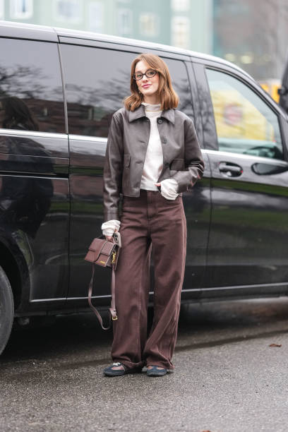 Guest wears black sunglasses, white long sleeve sweater, dark brown cropped leather jacket, dark brown loose denim jean pants, shiny dark brown...