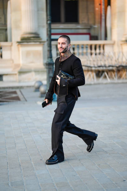 Guest wears black tailored coat, shiny black leather bag, black pants, shiny black leather shoes , outside Louis Vuitton, during the Paris Fashion...