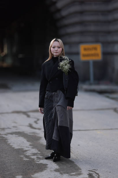 Guest wears black turtleneck sweater, black cropped blazer jacket / short cost, grey denim shoulder bag with white flowers inside, grey denim / jeans...