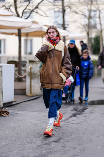 Guest wears bright cherry red burgundy scarf, dark brown oversized shearling aviator suede leather jacket, bright blue baggy denim jeans, white...