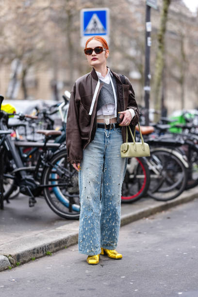 Guest wears bright orange hair, dark brown sunglasses, gold earrings, white buttoned up long sleeve cropped shirt, dark gray v-neck long sleeve...