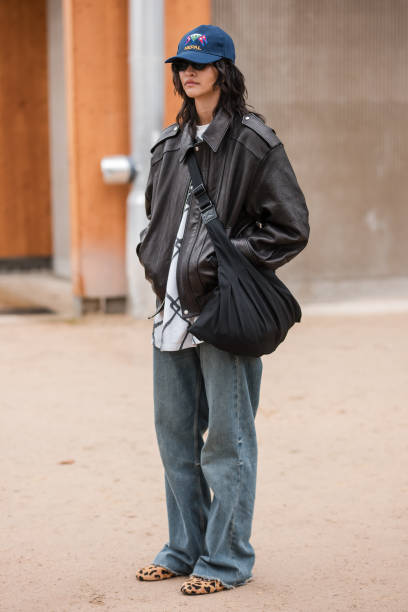 Guest wears brown leather jacket, baggy jeans, blue hat, leopard print flat shoes, outside Chanel, during the Haute Couture Spring/Summer 2024 as...