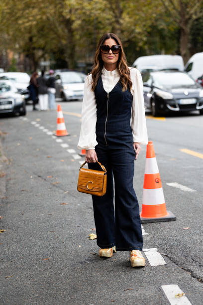 Guest wears brown sunglasses, a white shirt, a blue jeans denim jumpsuit, beige mules and a brown leather Chloé bag outside Chloé show during...