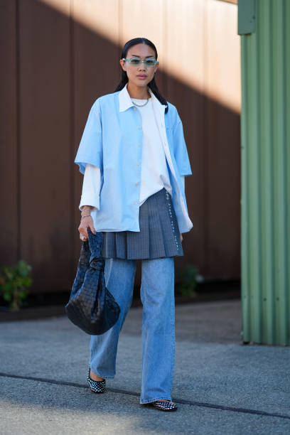 Guest wears clear green sunglasses, silver chain necklace, white long sleeve shirt, light blue short sleeve unbuttoned shirt, navy blue pleated mini...