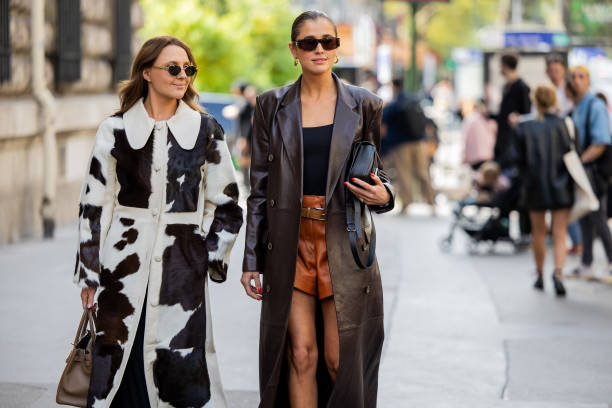 Guest wears cow print coat, brown bag & Darja Barannik wears brown leather short, brown shorts, black top, black bag outside Hermes during the...