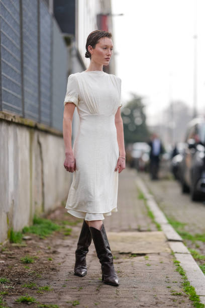 Guest wears cream short sleeve dress, shiny dark brown cowboy boots leather shoes, outside Jil Sander, during the Milan Fashion week Women's...