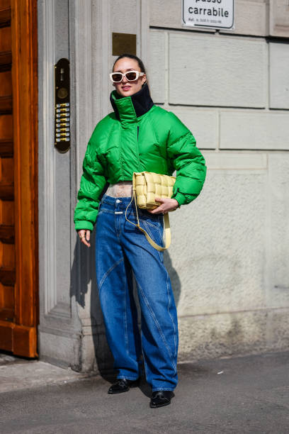 Guest wears cream sunglasses, a green bomber jacket, a light yellow leather quilted bag, blue denim jeans / pants, black leather shoes, outside...