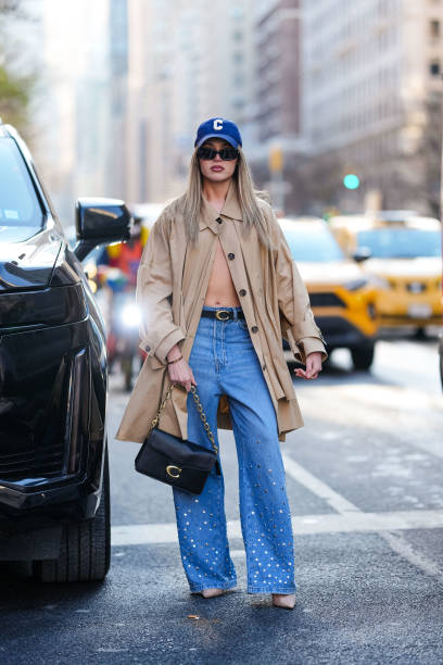 Guest wears dark blue Coach baseball cap hat, light brown Coach wind coat, black leather Coach belt, navy blue high waisted flared silver...