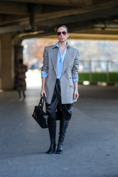 Guest wears dark brown aviator sunglasses, gold earrings, light blue oversized half buttoned long sleeve shirt, light gray white pinstripe double...