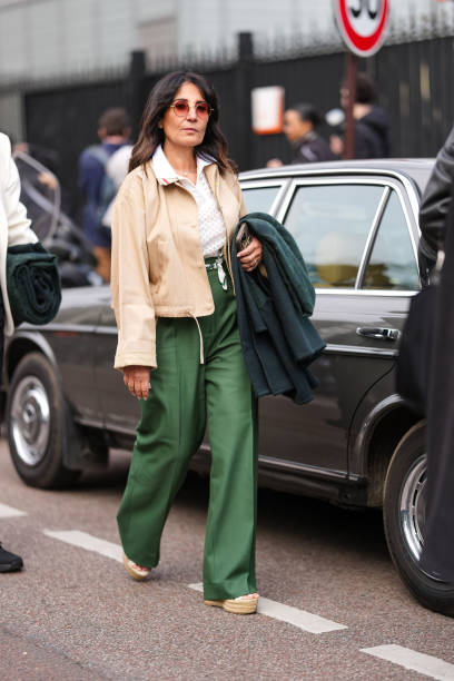 Guest wears dark brown sunglasses, white sheer mesh pattern polo Lacoste shirt, silver necklace, light brown unbuttoned jacket, dark green high...