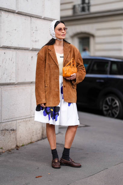 Guest wears dark brown sunglasses, white textured cap, dark brown suede oversized Miu Miu blazer jacket, cream tank top, white loose purple floral...