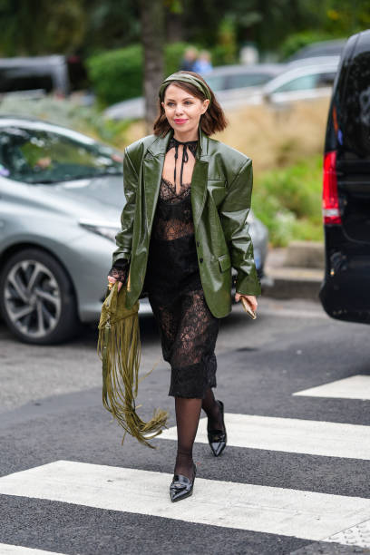 Guest wears dark green olive headband, shiny dark green olive oversized blazer jacket, black sheer mesh lace midi dress, dark green tassel bag, black...