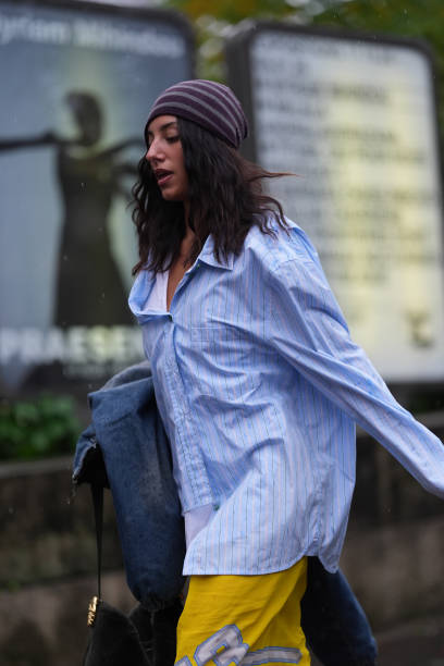Guest wears dark red gray pattern hat, navy blue denim jean coat I'm hand, light blue white lined buttoned up long sleeve oversized shirt, bright...