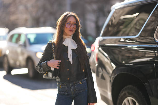 Guest wears dark red sunglasses, white bow long sleeve shirt, shiny black buttoned up cropped leather jacket, shiny black Coach leather bag, navy...