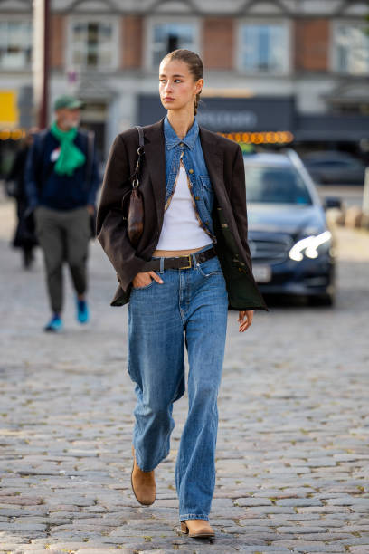 Guest wears denim jeans, shirt, brown oversized blazer outside Ganni during the Copenhagen Fashion Week Spring/Summer 2024 on August 10, 2023 in...