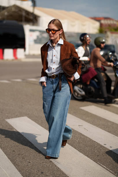 Guest wears denim wide leg jeans, a brown jacket, a bag, a blue button shirt is seen outside Prada show during the Milan Fashion Week Menswear...