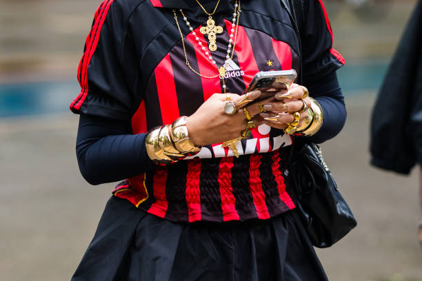 Guest wears football jersey, red and black vertical stripes, layered long-sleeve top, gold statement bracelets, stacked rings, gold cross necklace,...
