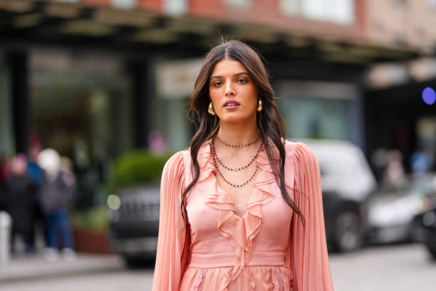 Guest wears gold earrings, black beaded layered necklaces, light pink long sleeve ruffled midi dress, outside Alice + Olivia, during the New York...