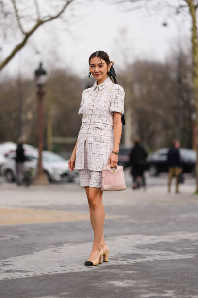 Guest wears gold earrings, dark brown braided hair with black bow, light pink pattern/print short sleeve buttoned light pink embellished Chanel...