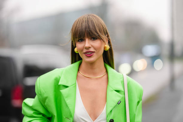 Guest wears gold earrings, gold necklace, white v-neck shirt, bright green oversized leather jacket, outside Gucci, during the Milan Fashion week...
